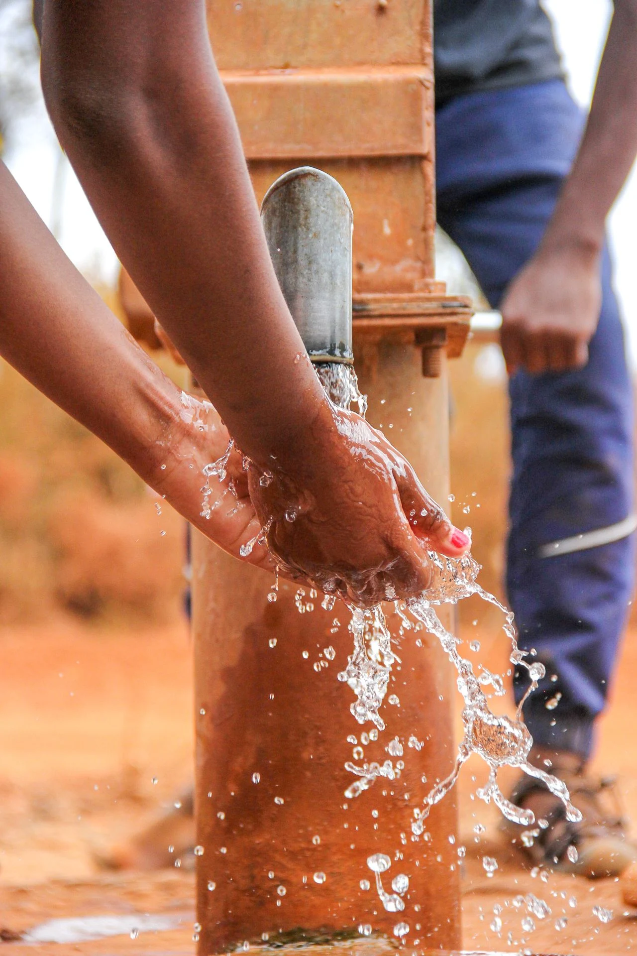 Hands drawing water from a borehole pump